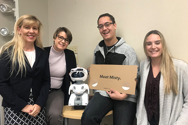 (left to right): Dr. Isabel Pedersen, Dr. Andrea Slane, and research assistants Jayden Cooper and Dallas Hill. They are accompanied by “Misty”, a robot designed to perform human-to-robot and robot-to-robot interactions using vision algorithms, supervised or autonomous control, and voice recognition.