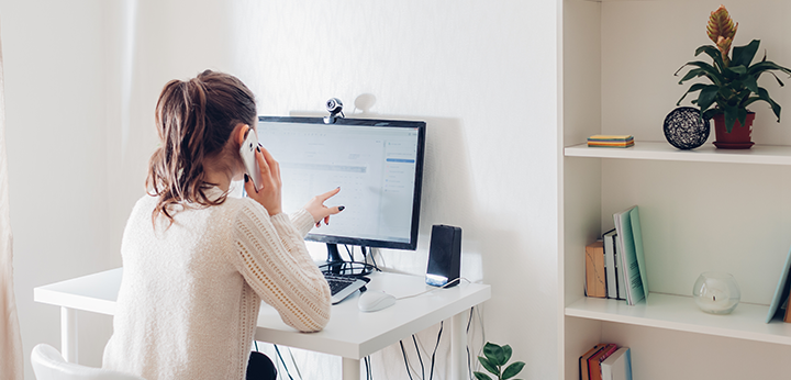 A woman sitting at her desk pointing at her computer while talking on the phone.